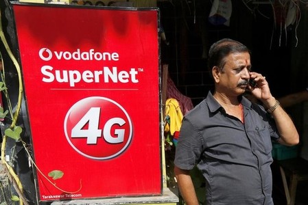 A man speaks on his mobile phone next to a Vodafone advertisement in Kolkata