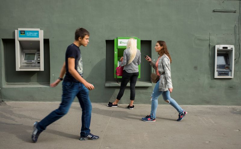 A woman uses an ATM machine as people walk past in central Kharkiv