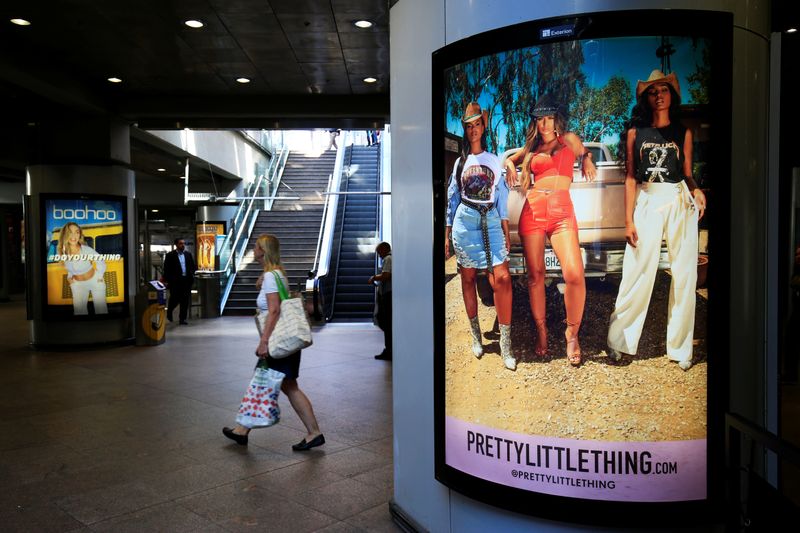 FILE PHOTO: A shopper walks pass advertising billboards for Boohoo and for 'Pretty Little Things', a Boohoo brand, at Canary Wharf DLR station in central London
