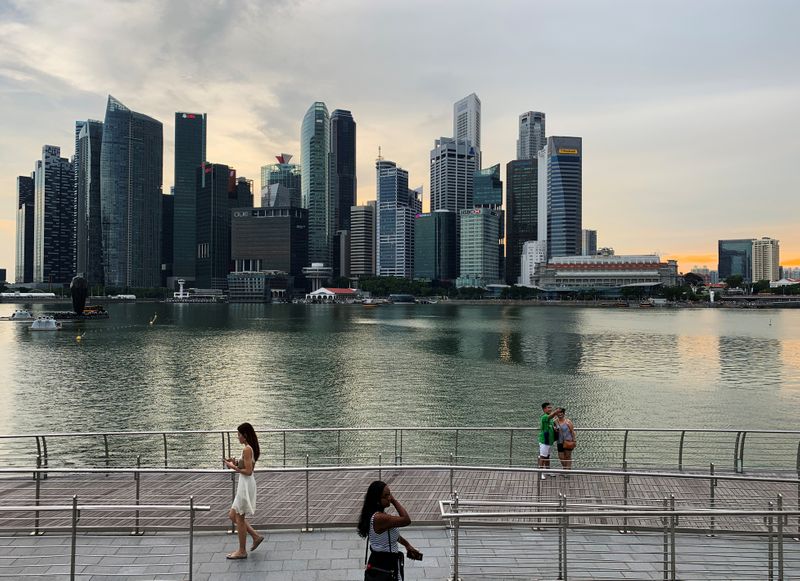 FILE PHOTO: Passersby hold their mobile phones to take selfies with Singapore's central business district skyline in the background