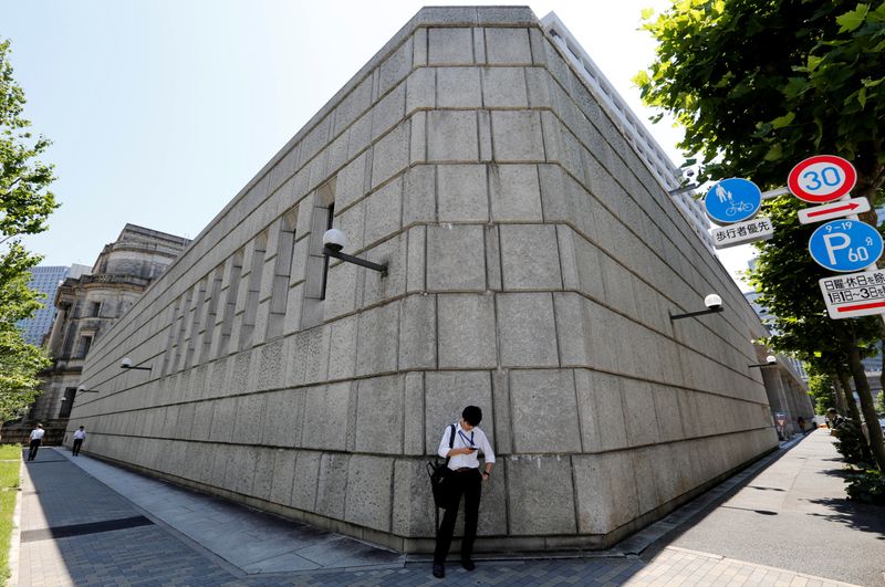 FILE PHOTO: A man looks at a mobile phone in front of the Bank of Japan building in Tokyo