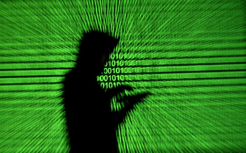 FILE PHOTO: Silhouette of mobile device user is seen next to a screen projection of binary code are seen in this picture illustration