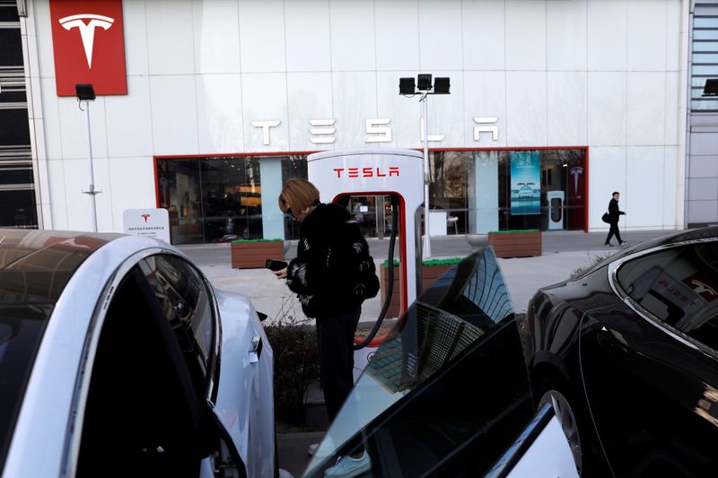 FILE PHOTO: Woman charges a Tesla car in front of the electric vehicle maker's showroom in Beijing