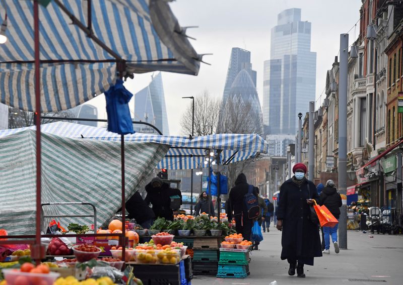FILE PHOTO: People shop at market stalls, with skyscrapers of the CIty of London, Britain financial district seen behind, in London
