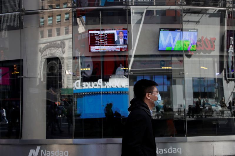 A man with a face mask walks by television screens outside the Nasdaq Market Site, after further cases of coronavirus were confirmed in New York, at Times Square in New York