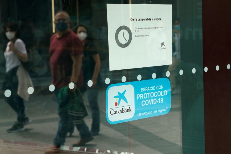 People walk past a closed Caixabank's branch during a one-day strike called by unions against the bank's plans for layoffs in Madrid