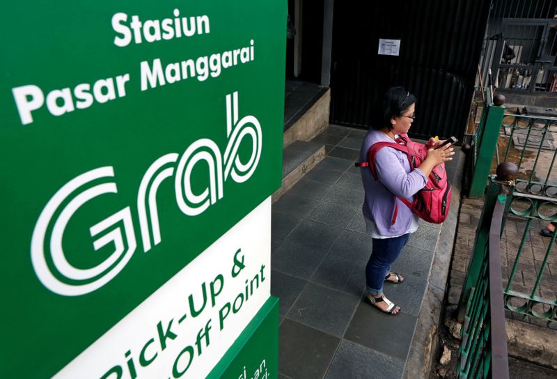 FILE PHOTO: A woman uses her phone near a sign for the online ride-hailing service Grab at the Manggarai train station in Jakarta