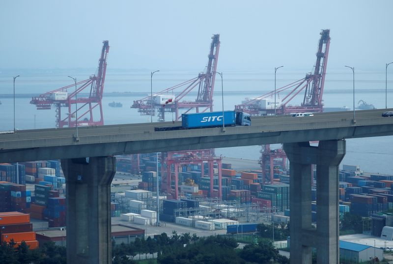 FILE PHOTO: A truck carrying a shipping container travels past cranes at Pyeongtaek port in Pyeongtaek