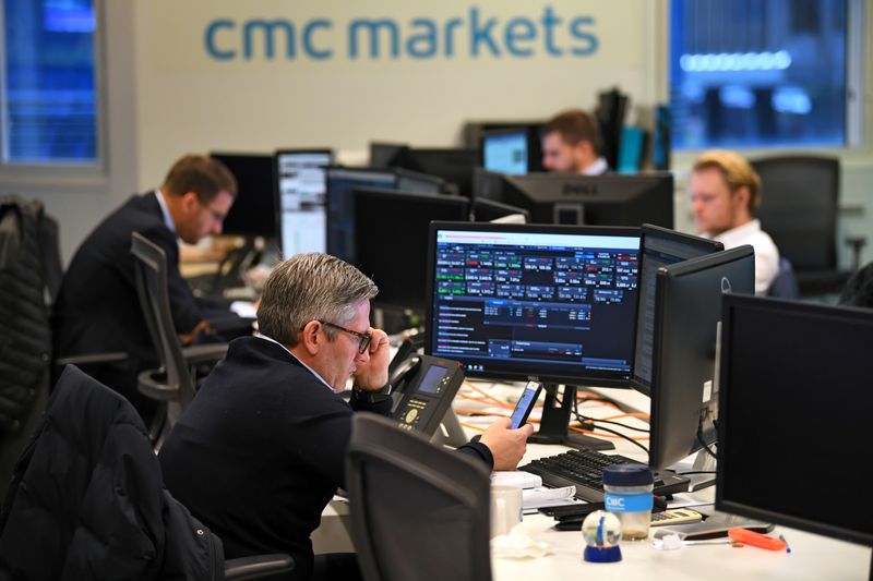 FILE PHOTO: Dealers work at their desks whilst screens show market data at CMC Markets in London