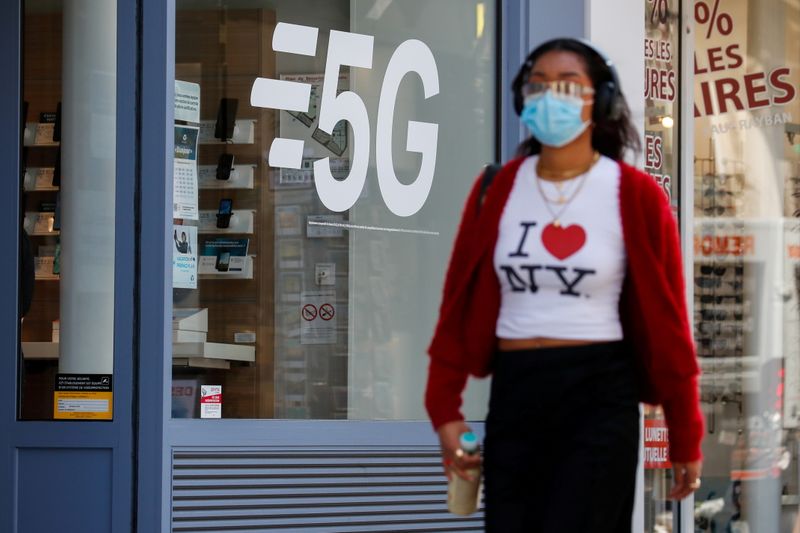 FILE PHOTO: A woman walks past a 5G data network sign at a mobile phone store in Paris