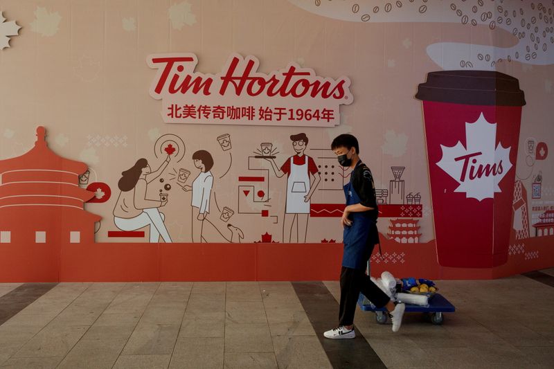 FILE PHOTO: A man walks past a store front poster advertising the opening of a cafe of the Canadian coffee and fastfood chain Tim Hortons in Beijing