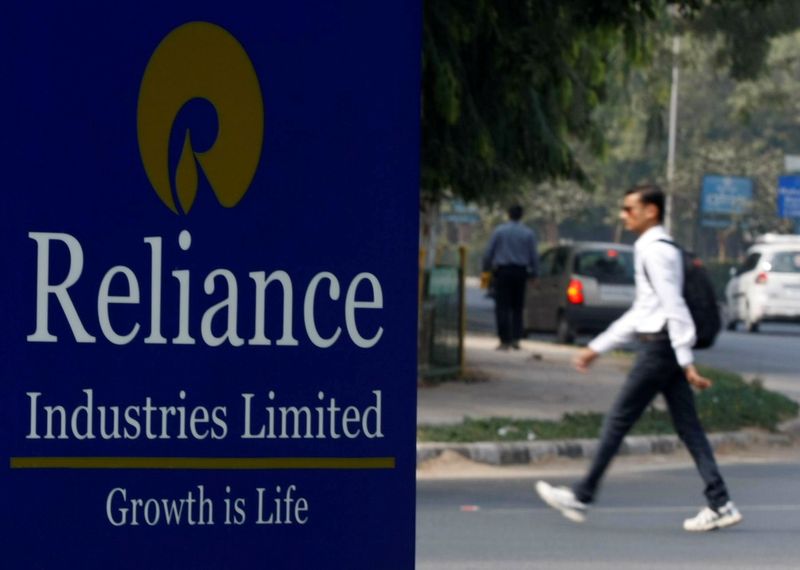 FILE PHOTO: A man walks past a Reliance Industries Limited sign board installed on a road divider in Gandhinagar