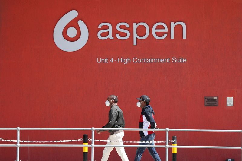 FILE PHOTO: People wearing face masks walk past a logo of South African pharmaceuticals company Aspen Pharmacare at its Johnson & Johnson COVID-19 vaccine facility in Gqeberha, South Africa