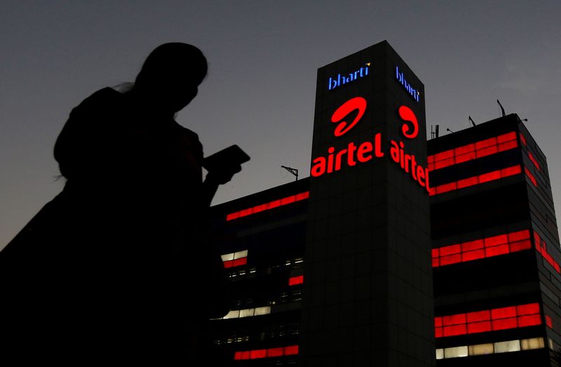 FILE PHOTO: A girl checks her mobile phone as she walks past the Bharti Airtel office building in Gurugram