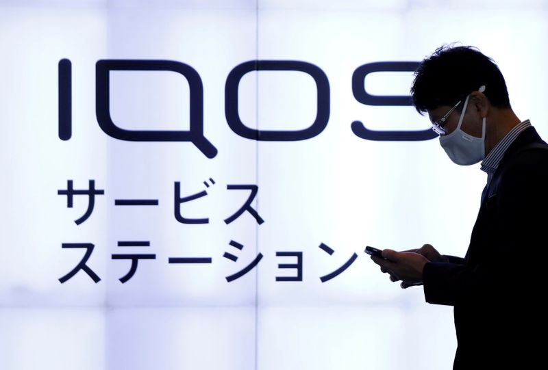FILE PHOTO: Man walks past a sign board of a service station for Philip Morris' iQOS heat-not-burn electronic cigarette on a street in Tokyo