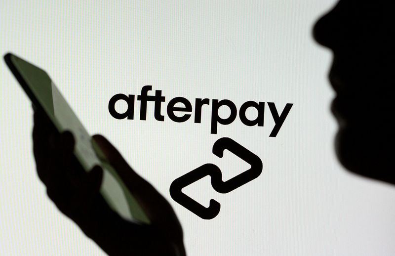 Woman with a smartphone is seen in front of a displayed Afterpay logo