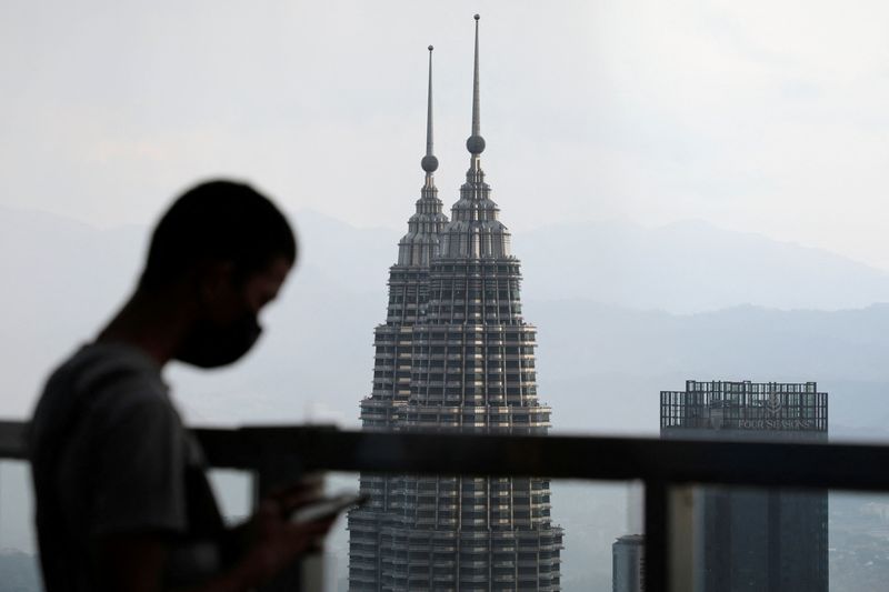 FILE PHOTO: A man wearing a protective mask uses his phone as the Petronas Twin Towers are seen in the background, in Kuala Lumpur