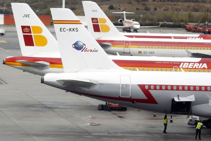 Staff stand under an Iberia airplane parked on the tarmac at Madrid's Barajas airport
