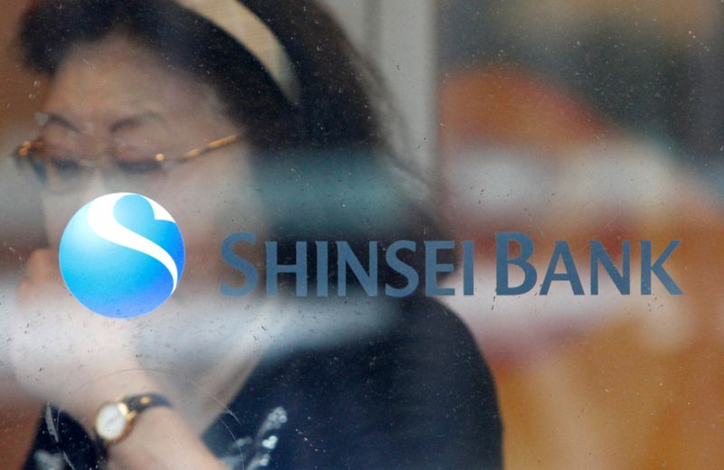 FILE PHOTO: A woman walks past a logo of the Shinsei Bank at its branch in Yokohama