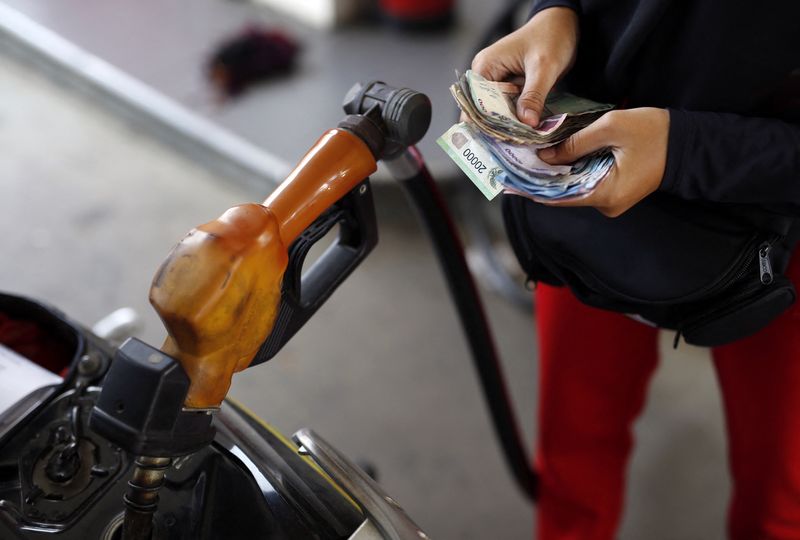 A worker at a state-owned Pertamina petrol station holds money as a motorcycle is filled with subsidised fuel in Jakarta