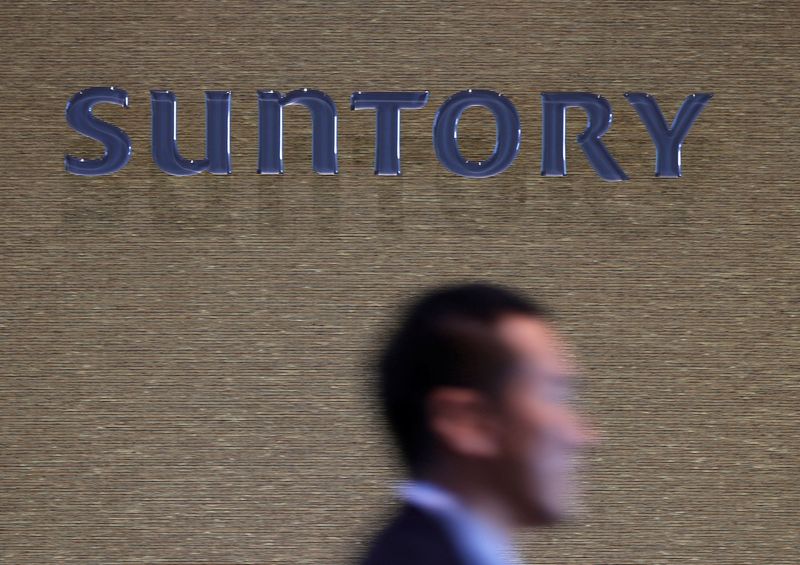 FILE PHOTO: Man walks past a signboard of Suntory Holdings at the entrance of Suntory World Headquarters in Tokyo