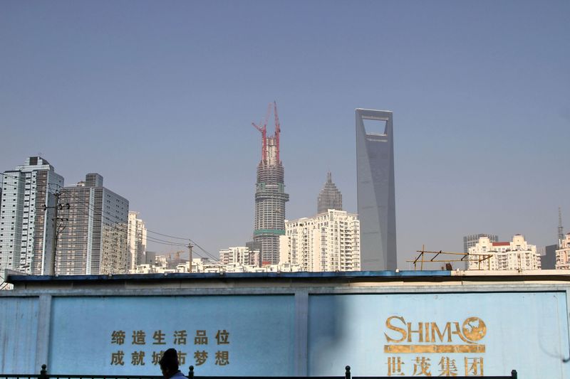 FILE PHOTO: Man walks past a wall carrying the logo of Shimao Group, with residential buildings and the financial district of Pudong seen in the background, in Shanghai