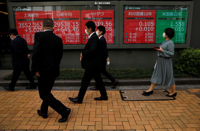 Passersby wearing protective face masks walk past an electronic board displaying world stock indexes in Tokyo