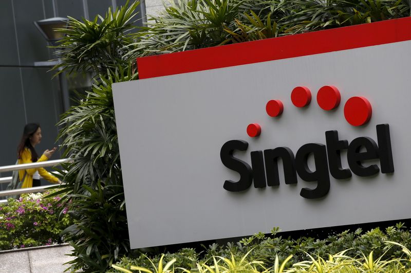A woman using a mobile phone walks behind a Singtel signage at their head office in Singapore