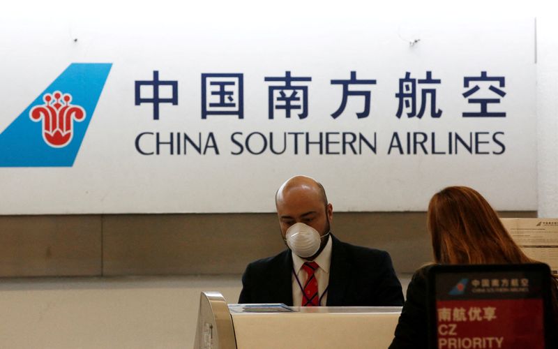 FILE PHOTO: A China Southern Airlines employee wears a surgical mask as a preventive measure in light of the coronavirus outbreak in China, while he attends a customer behind the counter at Benito Juarez international airport in Mexico City