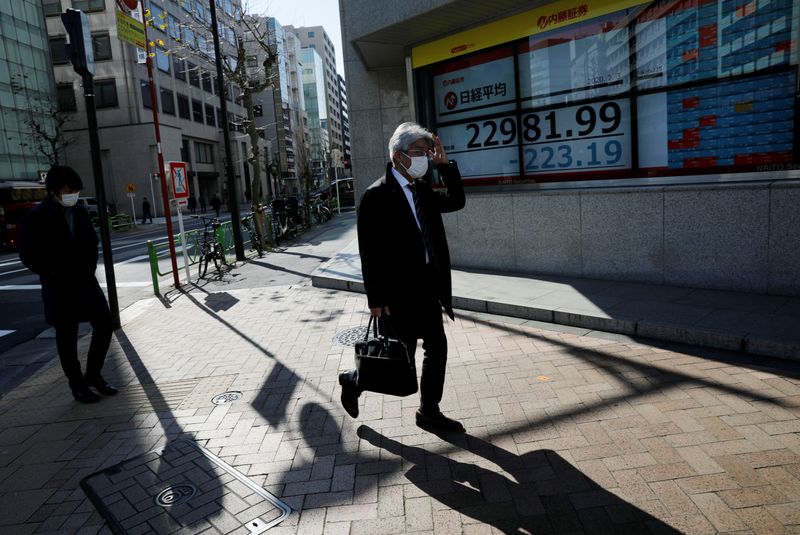 FILE PHOTO: People wearing surgical masks walk past a screen showing Nikkei index outside a brokerage in Tokyo