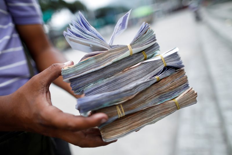 FILE PHOTO: The assistant of a bus driver holds Bolivar banknotes, worth between 0.01 and 0.25 US Dollars, after Venezuela's central bank announced it will cut six zeros from prices, in Caracas