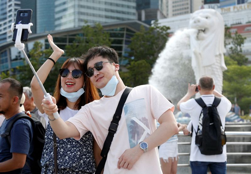 FILE PHOTO: Tourists wearing protective face masks pose for photos at the Merlion Park in Singapore