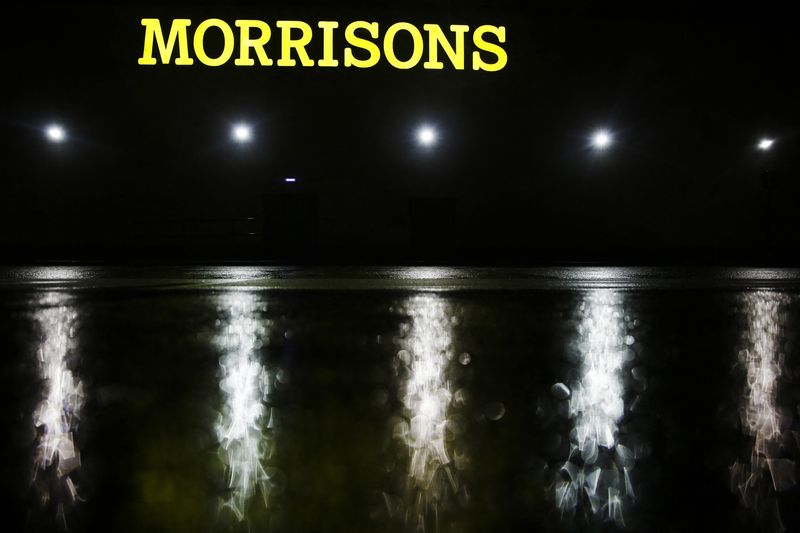 The illuminated logo shines above the wet car park of a Morrisons supermarket store in Croydon