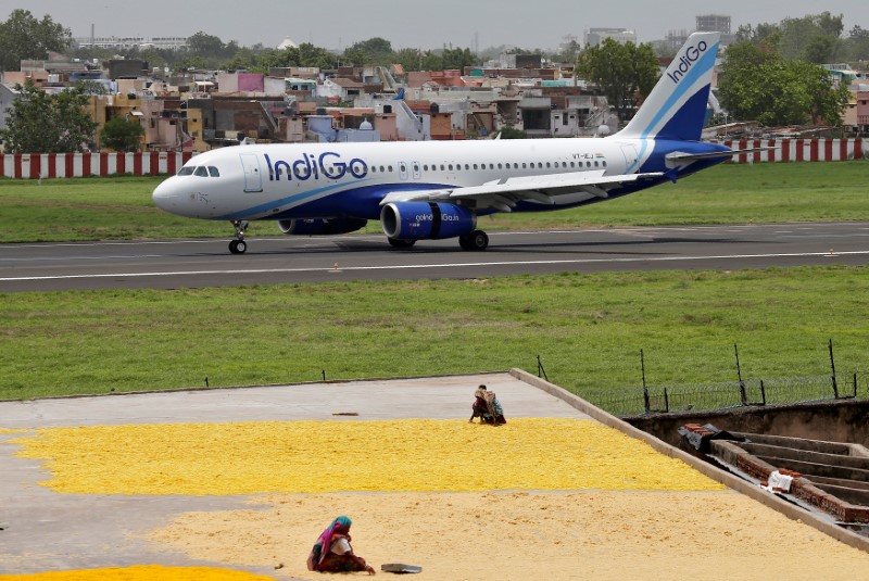 Women spread fryums for drying on a rooftop as an IndiGo Airlines Airbus A320 aircraft moves on the runway after landing at the Sardar Vallabhbhai Patel international airport in Ahmedabad