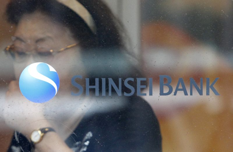 A woman walks past a logo of the Shinsei Bank at its branch in Yokohama