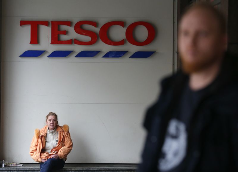 Woman sits under a logo of Tesco supermarket in Budapest