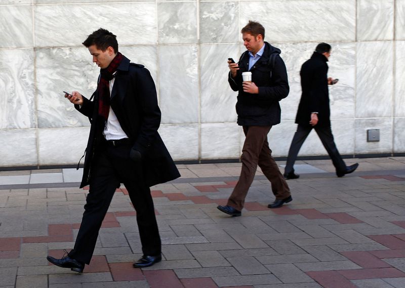 FILE PHOTO: People look at their phones while walking at the Canary Wharf business district in London