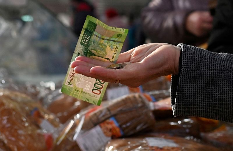 FILE PHOTO: A customer hands over Russian rouble banknotes and coins to a vendor at a market in Omsk