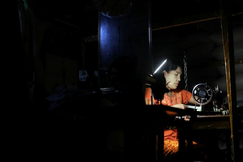 FILE PHOTO: A woman works on her sewing machine with mobile lighting during a power outage in Yangon