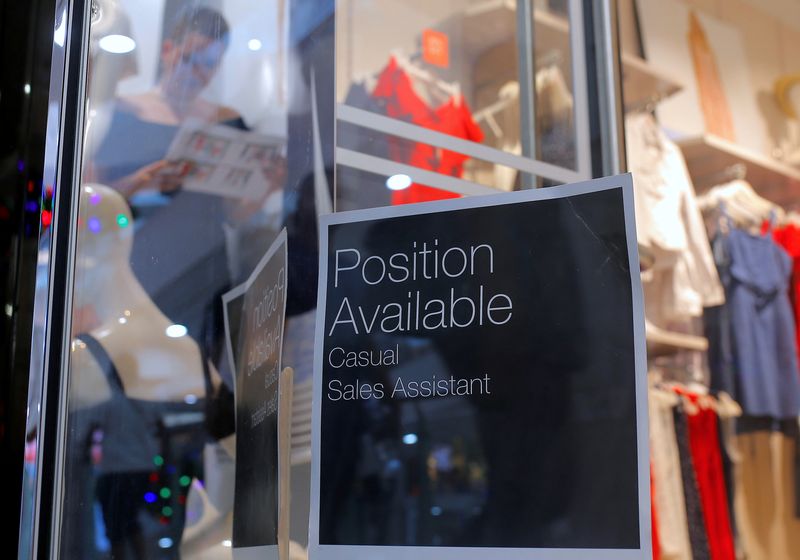 A sales assistant is seen seen through the window of a retail store displaying a job vacancy sign in central Sydney, Australia