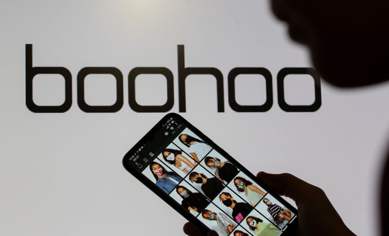 FILE PHOTO: A woman poses with a smartphone showing the Boohoo app in front of the Boohoo logo on display in this illustration