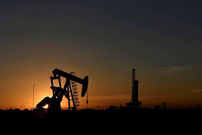 Imagen de archivo de un balancín operando frente a una plataforma de perforación durante una puesta de sol en un campo petrolero en Midland