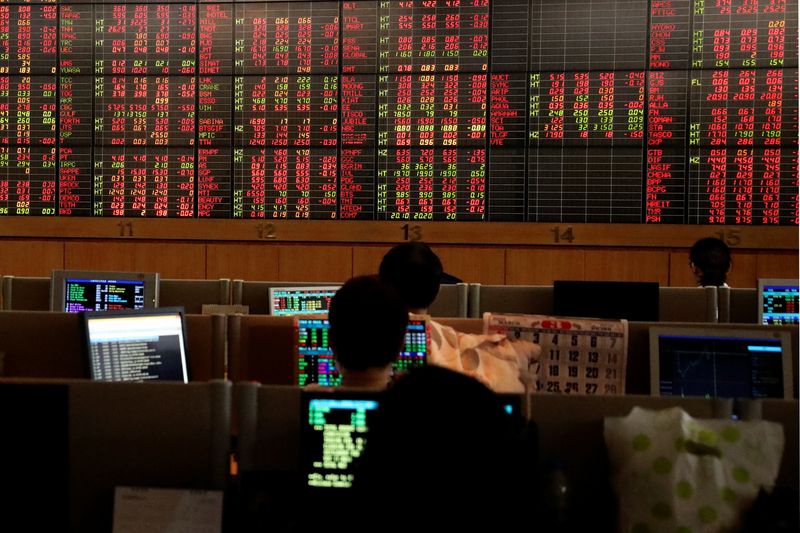FILE PHOTO: Traders are seen in front of a screen with trading figures in red at Thailand Stock Exchange building in Bangkok
