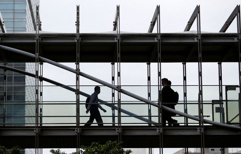 FILE PHOTO: Businessmen wearing protective face masks walk on a pedestrian bridge in a business district in Tokyo