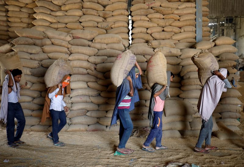 Workers carry sacks of wheat for sifting at a grain mill on the outskirts of Ahmedabad