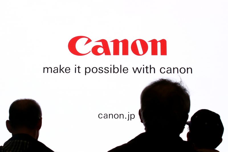 People are silhouetted against a display of the Canon brand logo at the CP+ camera and photo trade fair in Yokohama