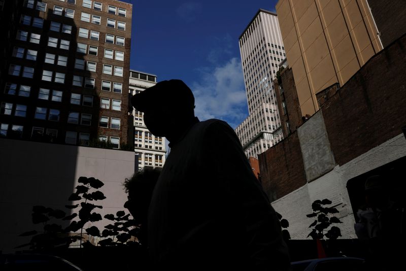 FILE PHOTO: A man is seen silhouetted wearing a protective face mask, amid the coronavirus disease (COVID-19) pandemic, walking near the financial district of New York City