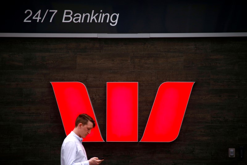 FILE PHOTO: A pedestrian looks at his phone as he walks past a logo for Australia's Westpac Banking Corp located outside a branch in central Sydney