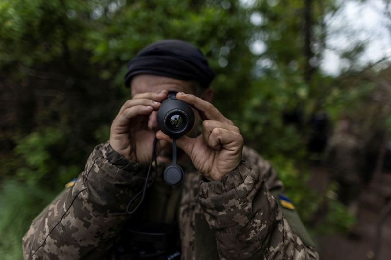 A service member of the Ukrainian armed forces uses a thermal monocular at an artillery position near Donetsk