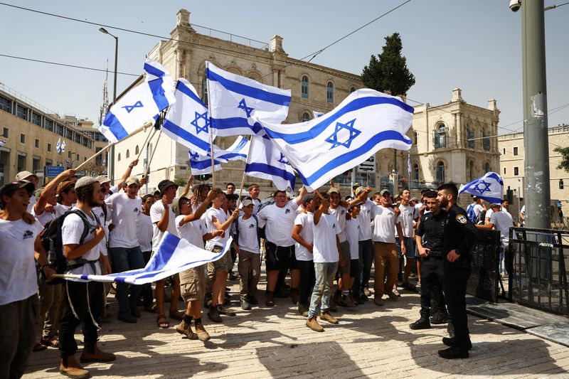 Israeli youths wave flags and sing as police stand guard before they start marching outside Jerusalem's Old City